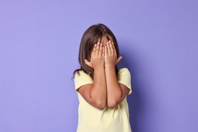 Photo of Scared little girl covering face with hands on violet background