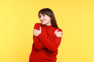 Photo of Young woman hugging himself on yellow background