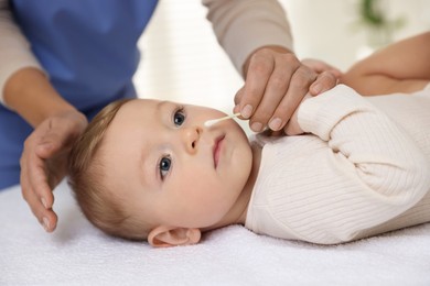 Photo of Pediatrician with cotton swab and cute little baby in clinic, closeup