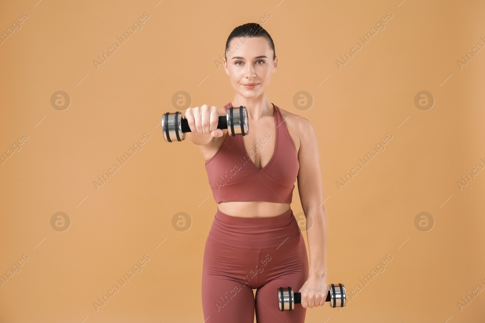 Photo of Woman exercising with dumbbells on beige background