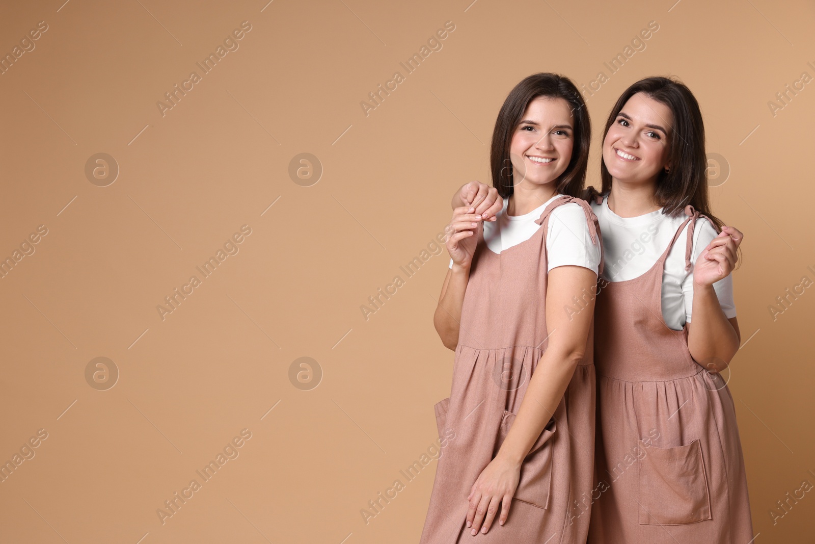 Photo of Portrait of happy twin sisters on pale brown background, space for text