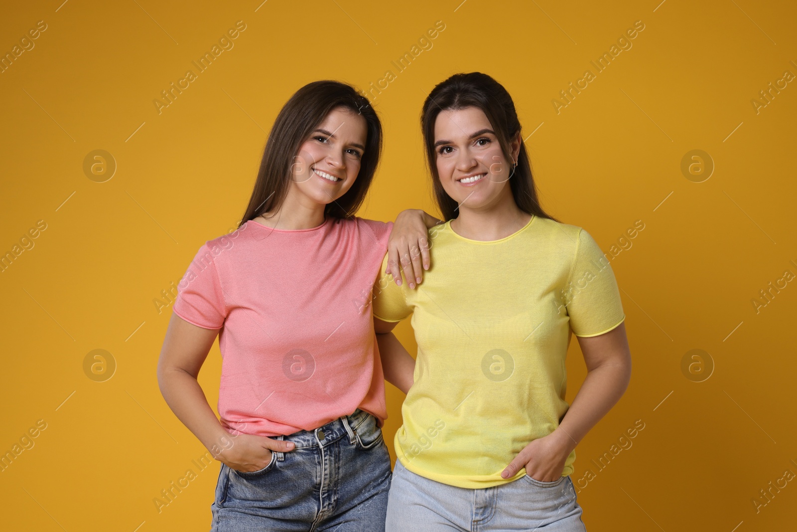 Photo of Portrait of happy twin sisters on orange background