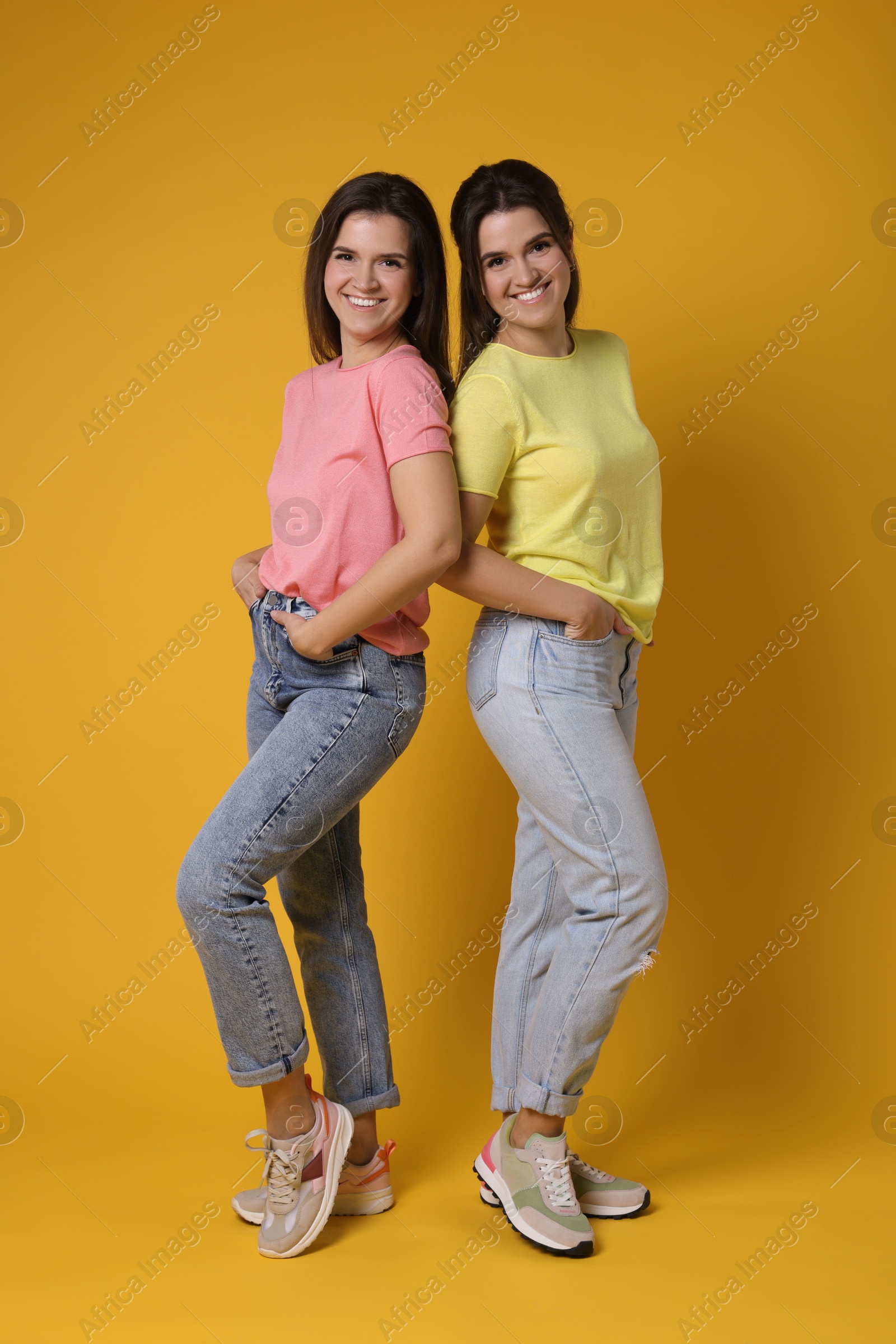 Photo of Portrait of happy twin sisters on orange background