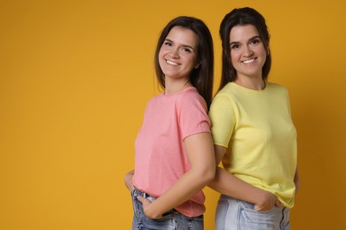 Photo of Portrait of happy twin sisters on orange background, space for text