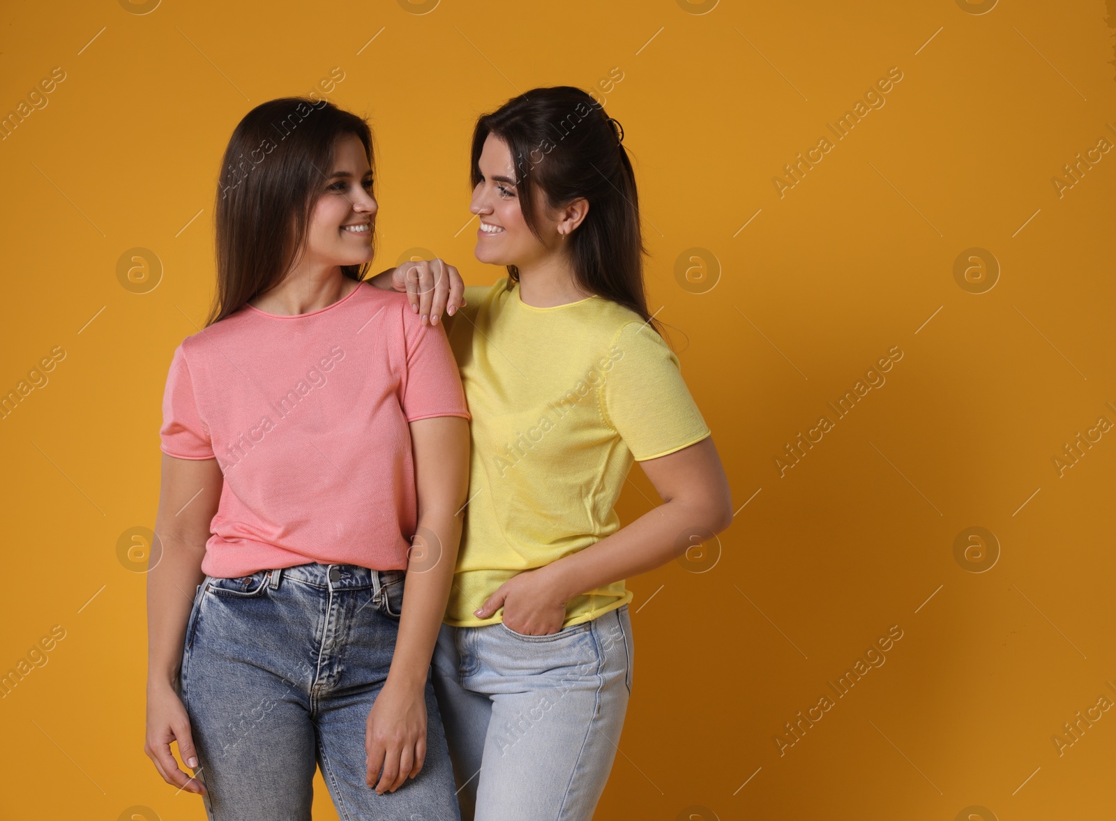 Photo of Portrait of happy twin sisters on orange background, space for text