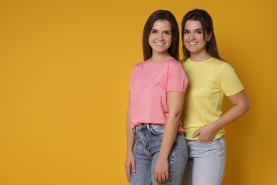 Photo of Portrait of happy twin sisters on orange background, space for text