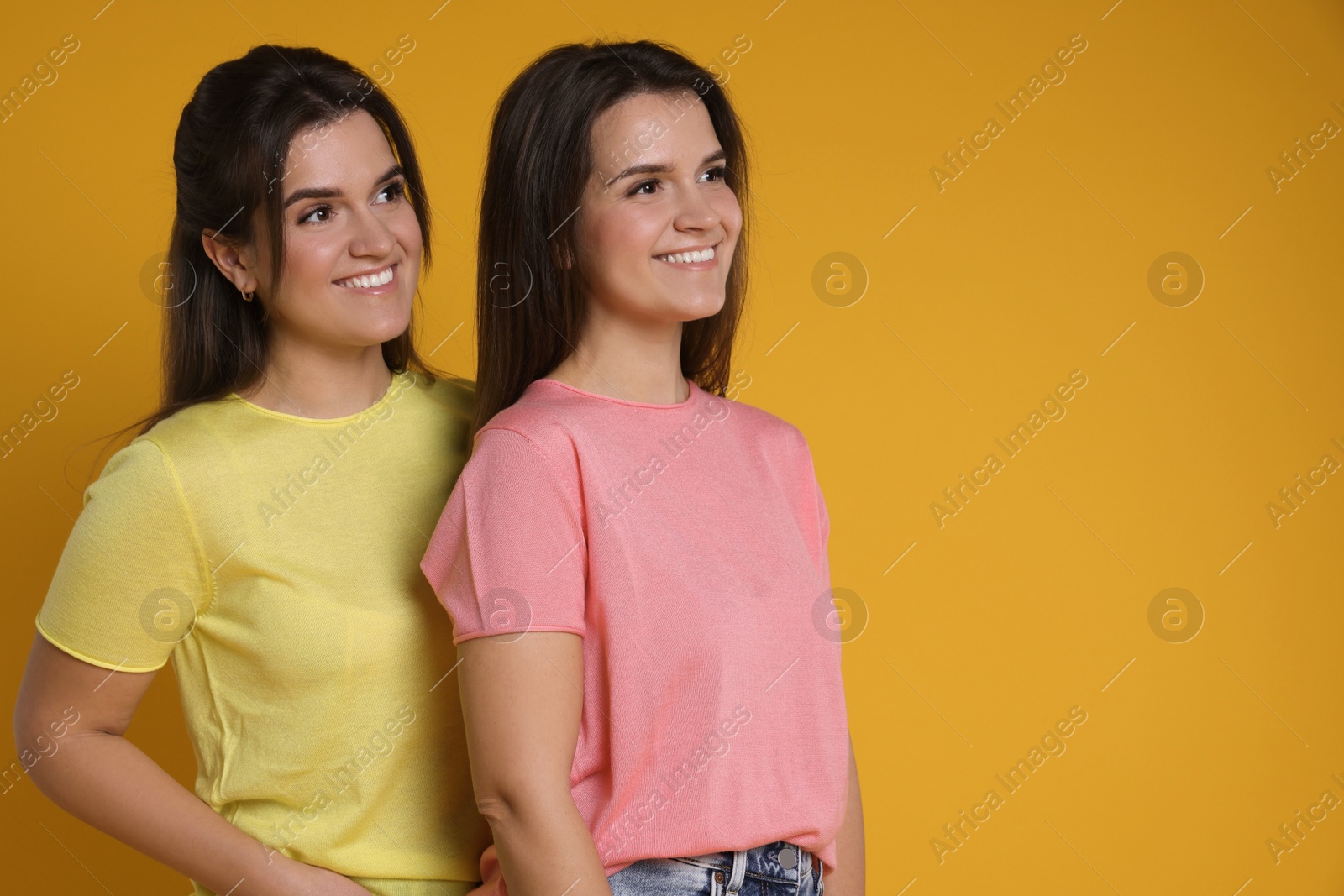 Photo of Portrait of happy twin sisters on orange background, space for text