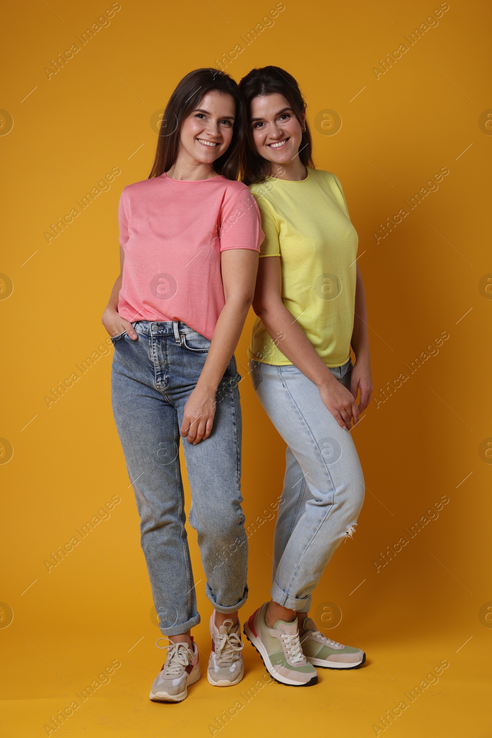 Photo of Portrait of happy twin sisters on orange background