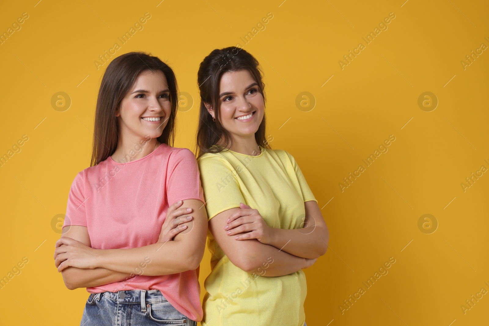 Photo of Portrait of happy twin sisters on orange background, space for text