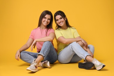 Photo of Portrait of happy twin sisters on orange background