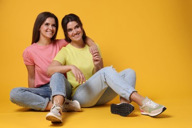 Photo of Portrait of happy twin sisters on orange background, space for text