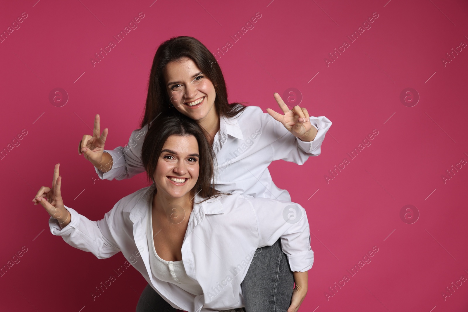 Photo of Beautiful twin sisters having fun on pink background, space for text