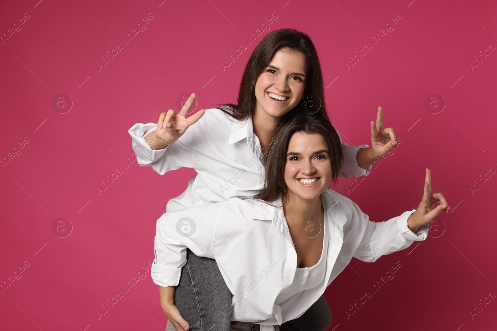 Photo of Beautiful twin sisters having fun on pink background