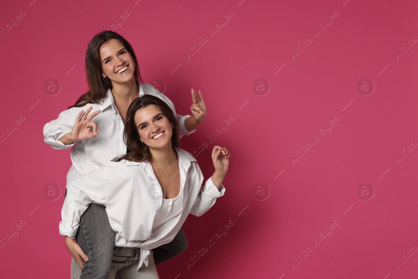 Photo of Beautiful twin sisters having fun on pink background, space for text