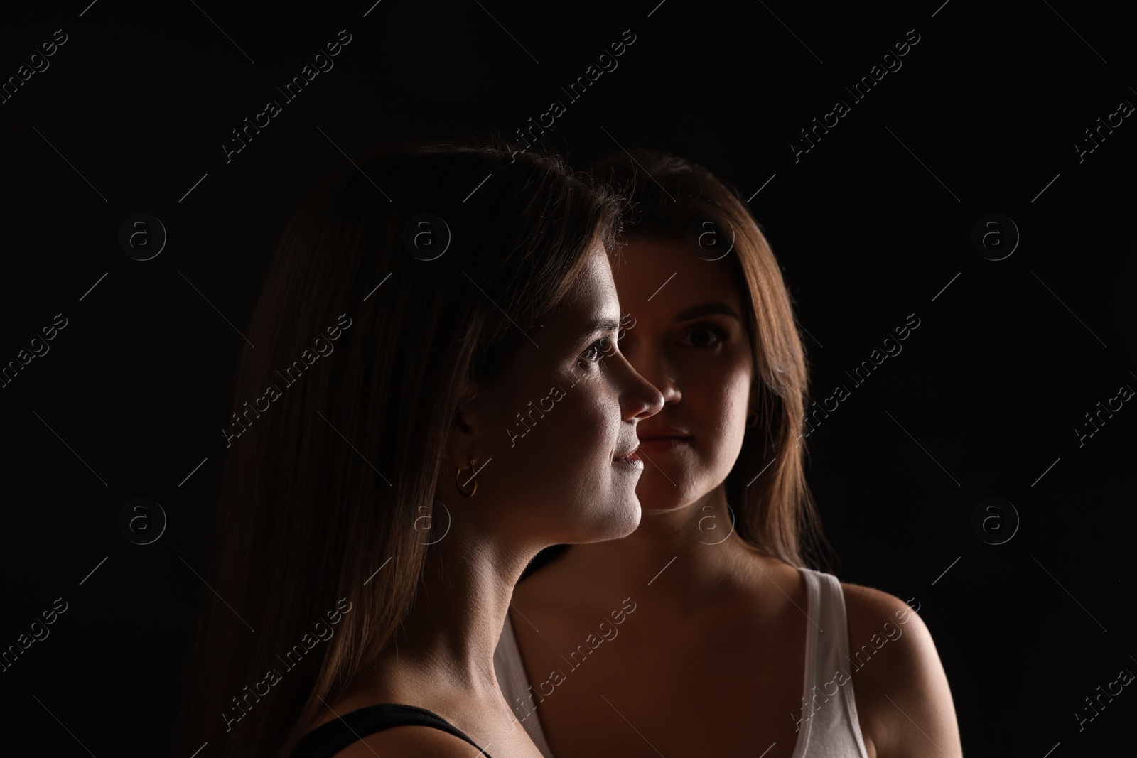 Photo of Portrait of beautiful twin sisters on black background