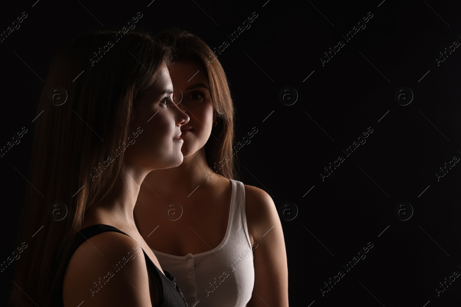 Photo of Portrait of beautiful twin sisters on black background, space for text