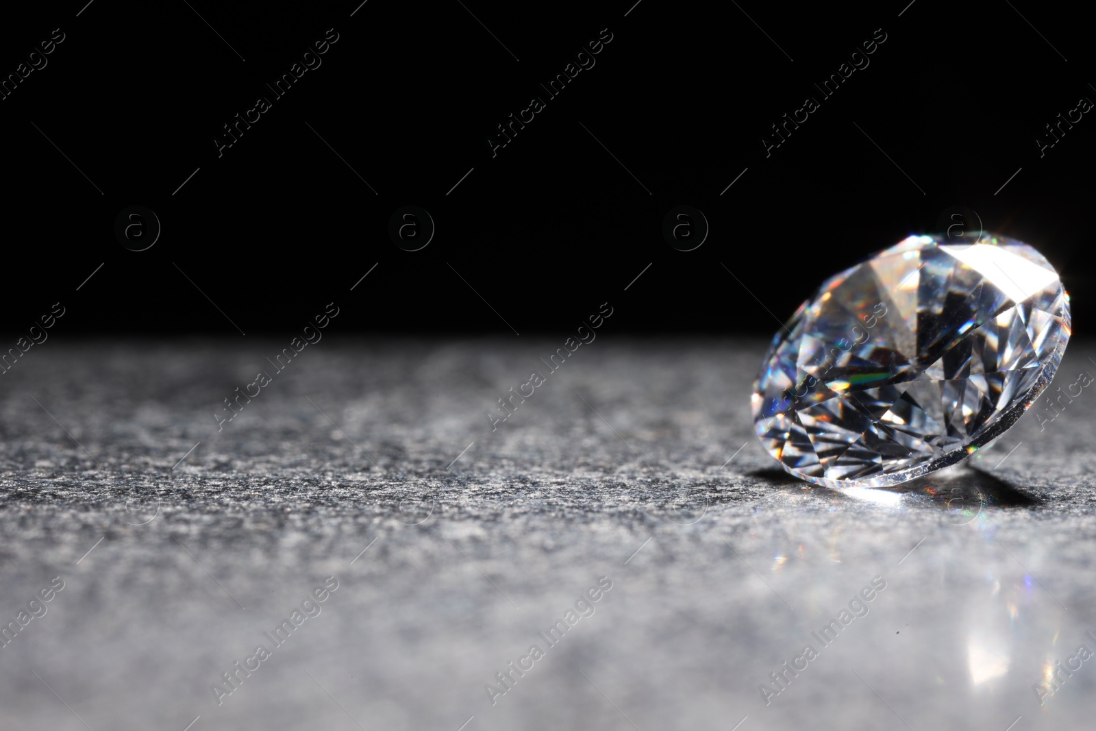 Photo of Beautiful shiny gemstone on stone against black background, space for text