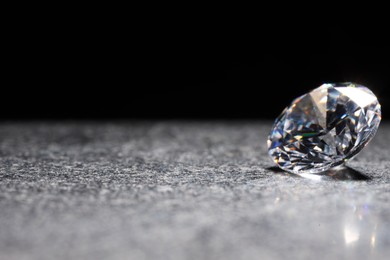 Photo of Beautiful shiny gemstone on stone against black background, space for text