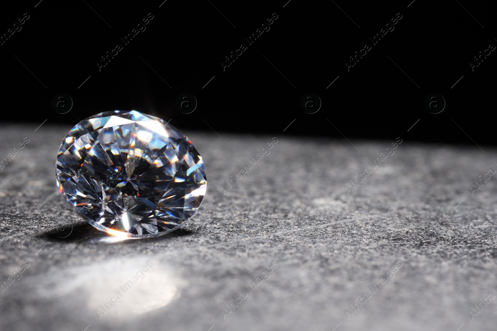 Photo of Beautiful shiny gemstone on stone against black background, space for text