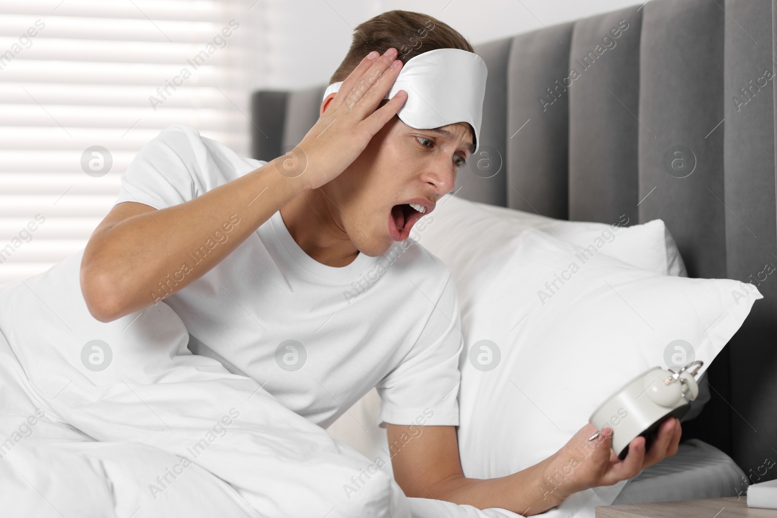 Photo of Overslept man with alarm clock in bed at home