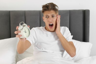 Photo of Overslept man with alarm clock in bed at home