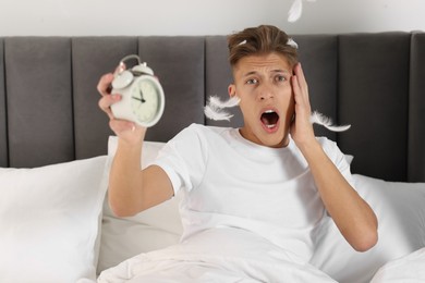 Photo of Overslept man with alarm clock in bed at home