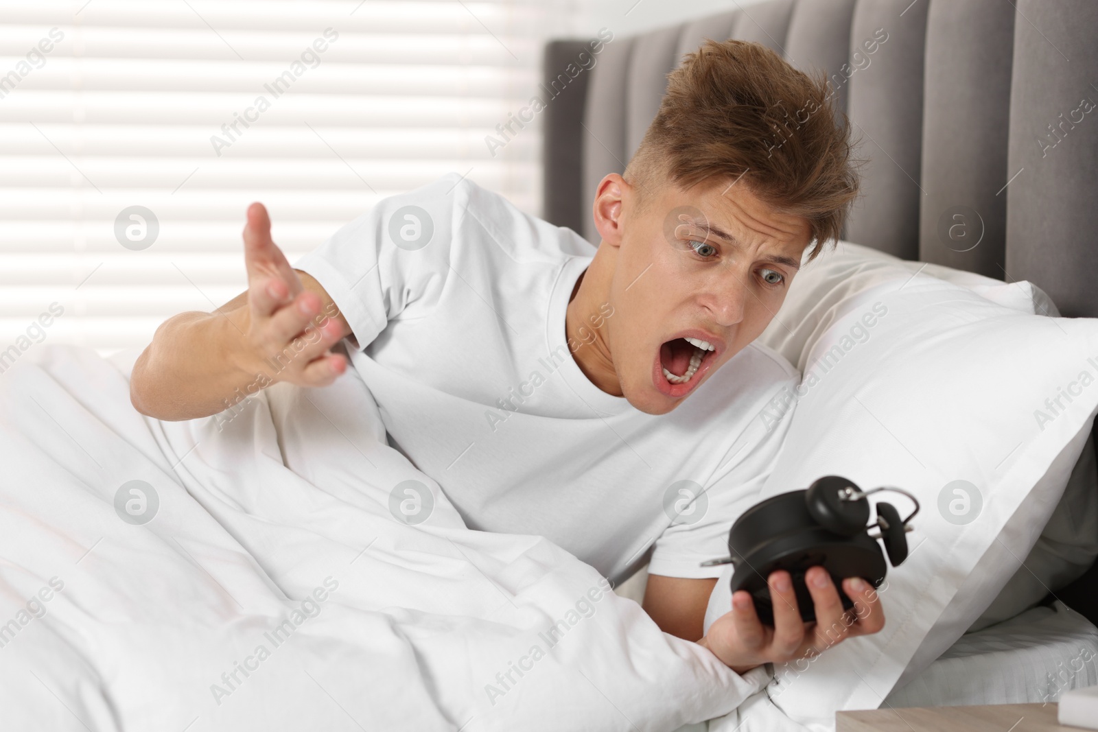 Photo of Overslept man with alarm clock in bed at home