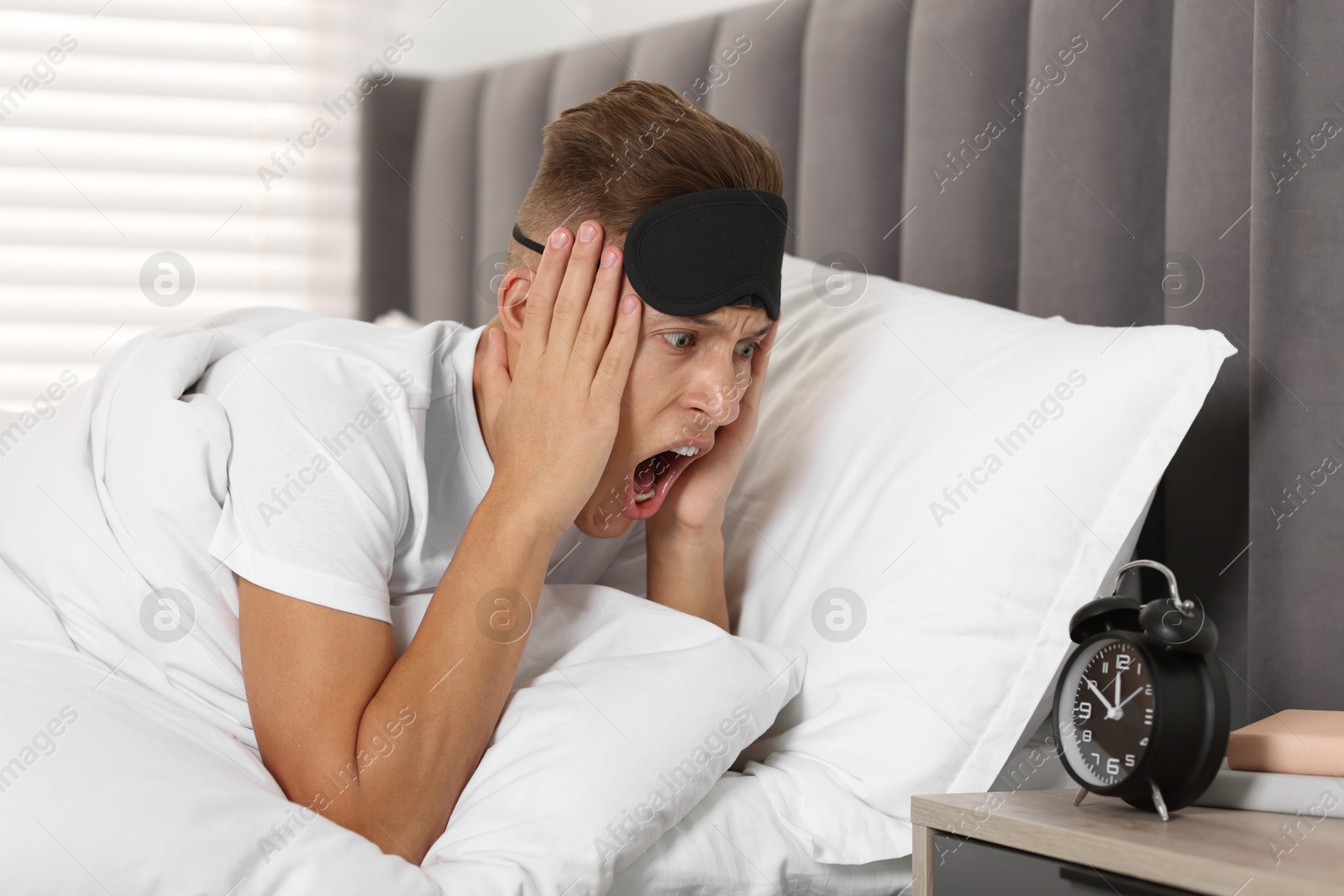 Photo of Overslept man with alarm clock in bed at home