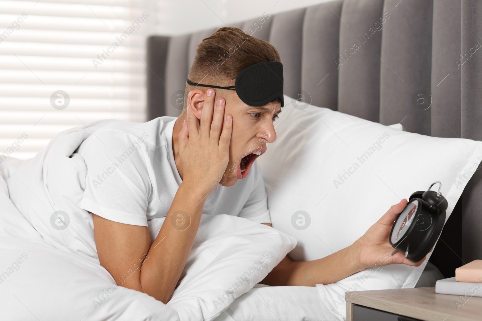 Photo of Overslept man with alarm clock in bed at home