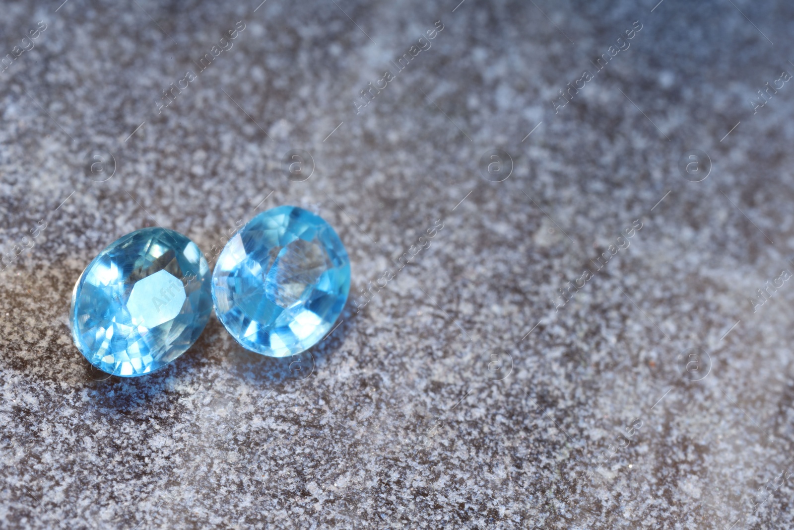 Photo of Beautiful shiny light blue gemstones on stone, space for text