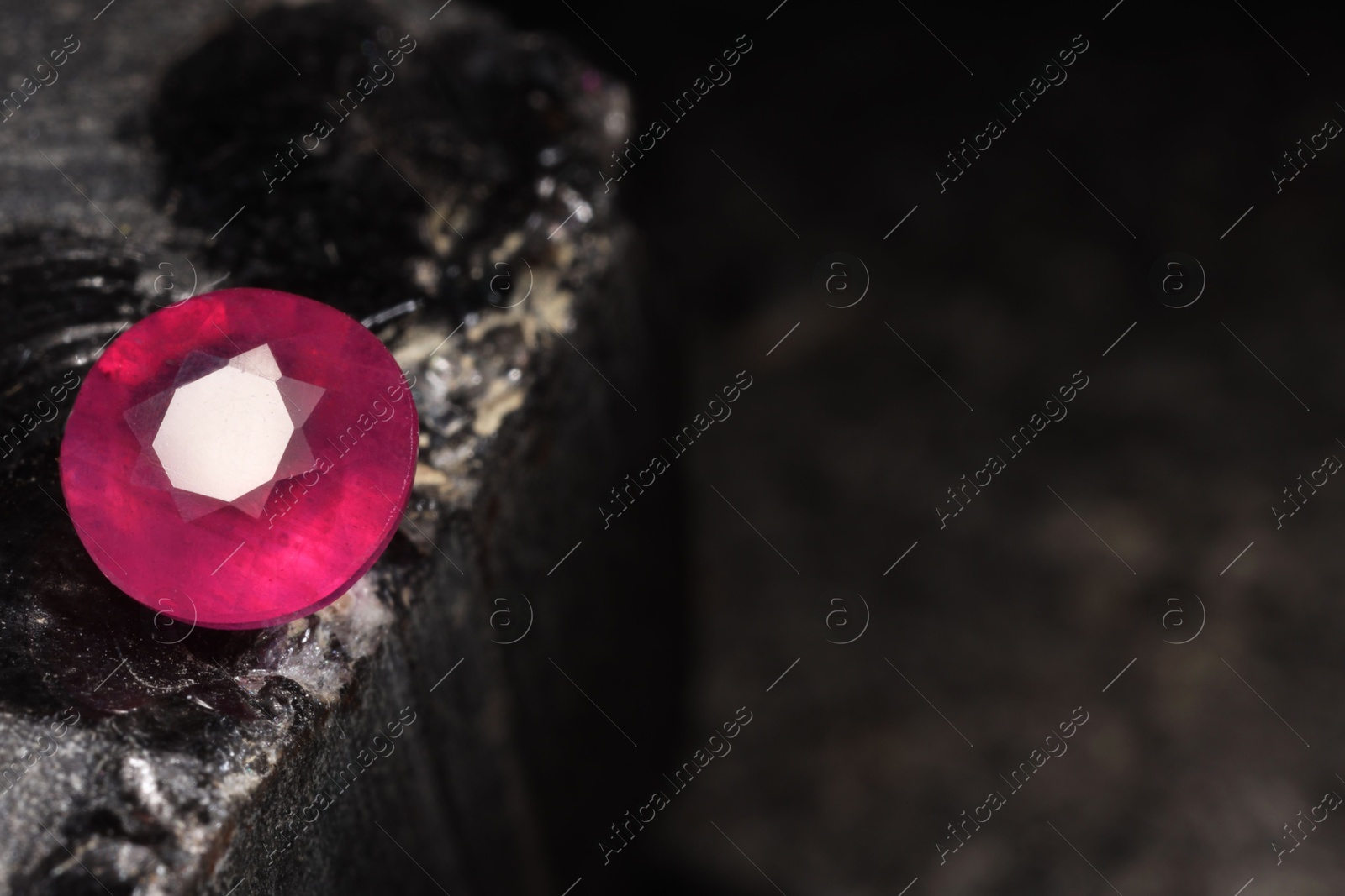 Photo of Beautiful shiny pink gemstone on stone, space for text