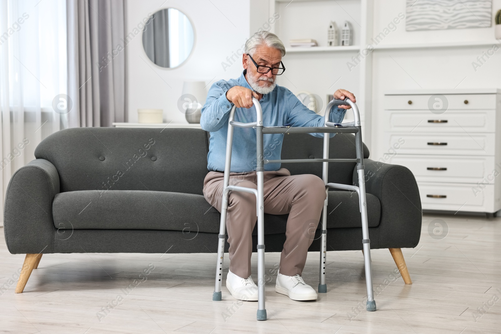 Photo of Senior man with walking frame on sofa at home