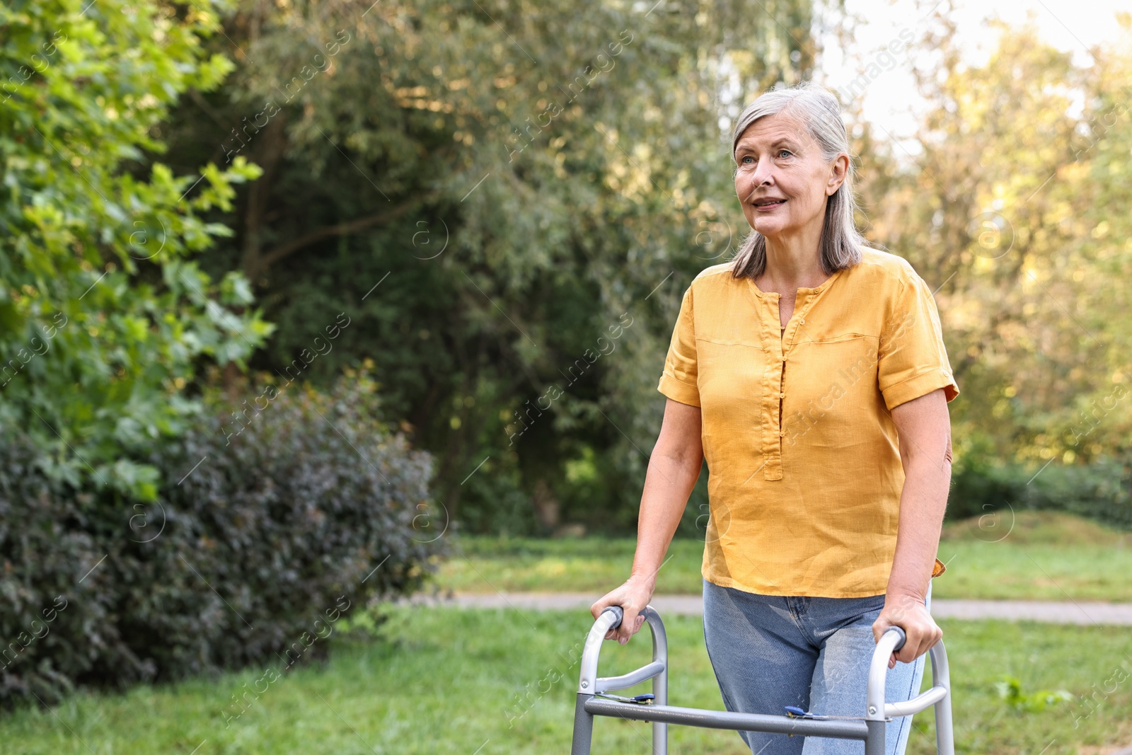 Photo of Senior woman with walking frame in park, space for text