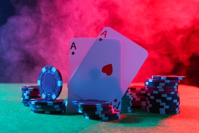 Photo of Poker chips and playing cards on green table in neon lights