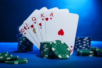 Poker chips and playing cards on blue table, closeup