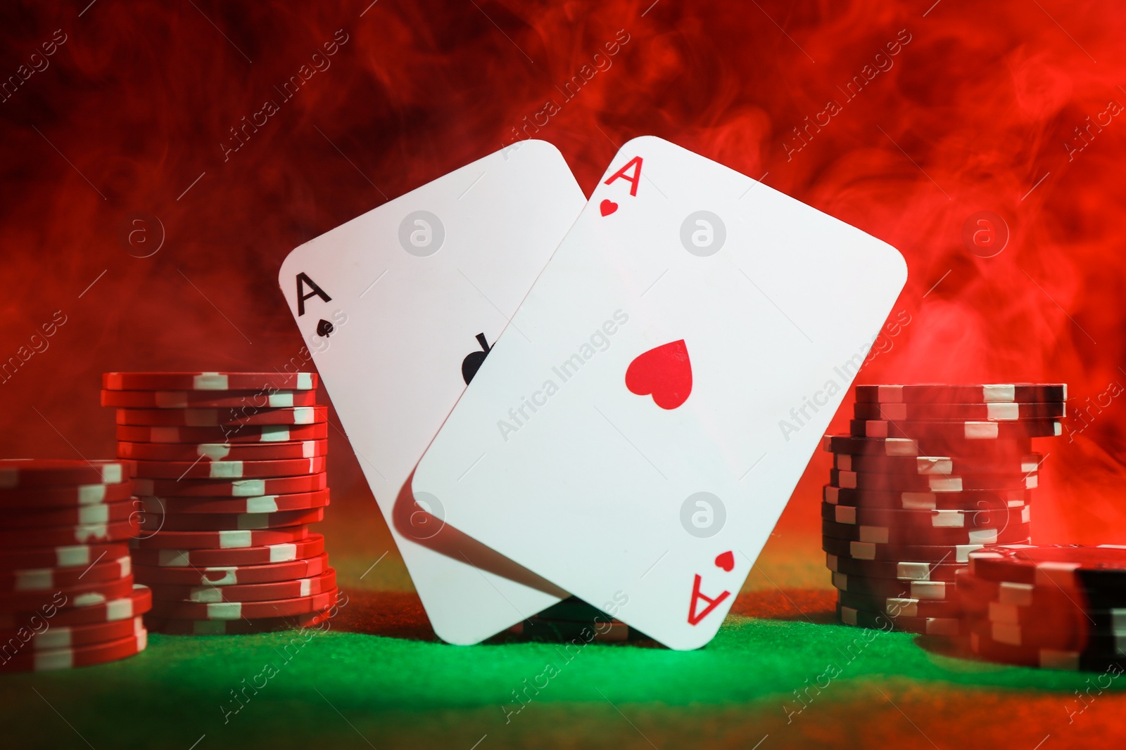 Photo of Poker chips and playing cards on green table in neon lights, closeup