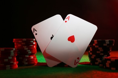 Photo of Poker chips and playing cards on green table in neon lights, closeup