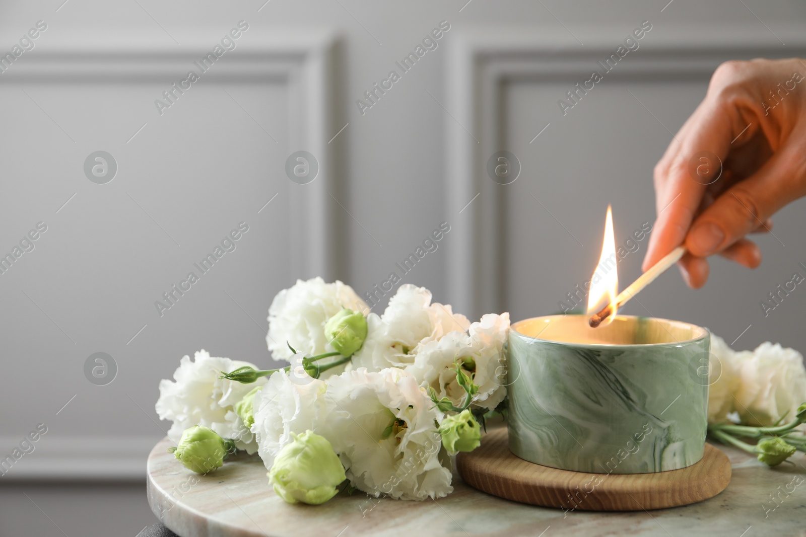 Photo of Woman lighting candle at table with beautiful flowers, closeup