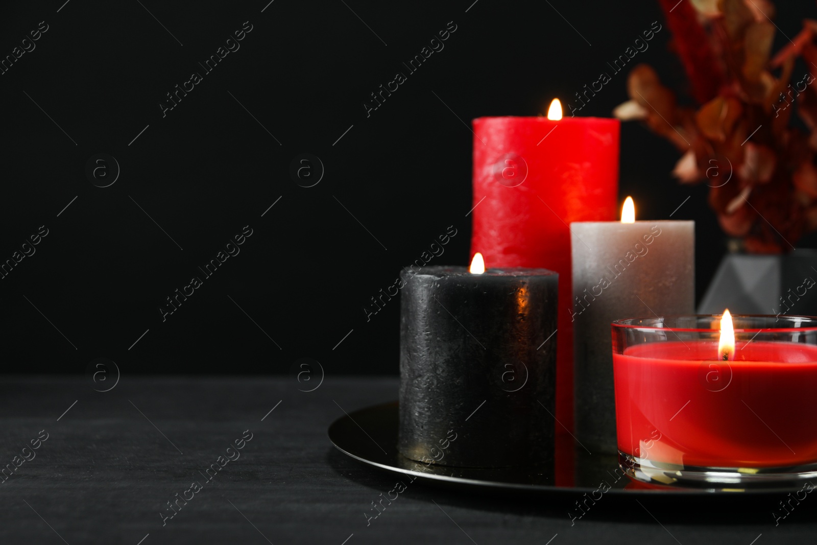 Photo of Beautiful burning candles and decor on black table, closeup. Space for text