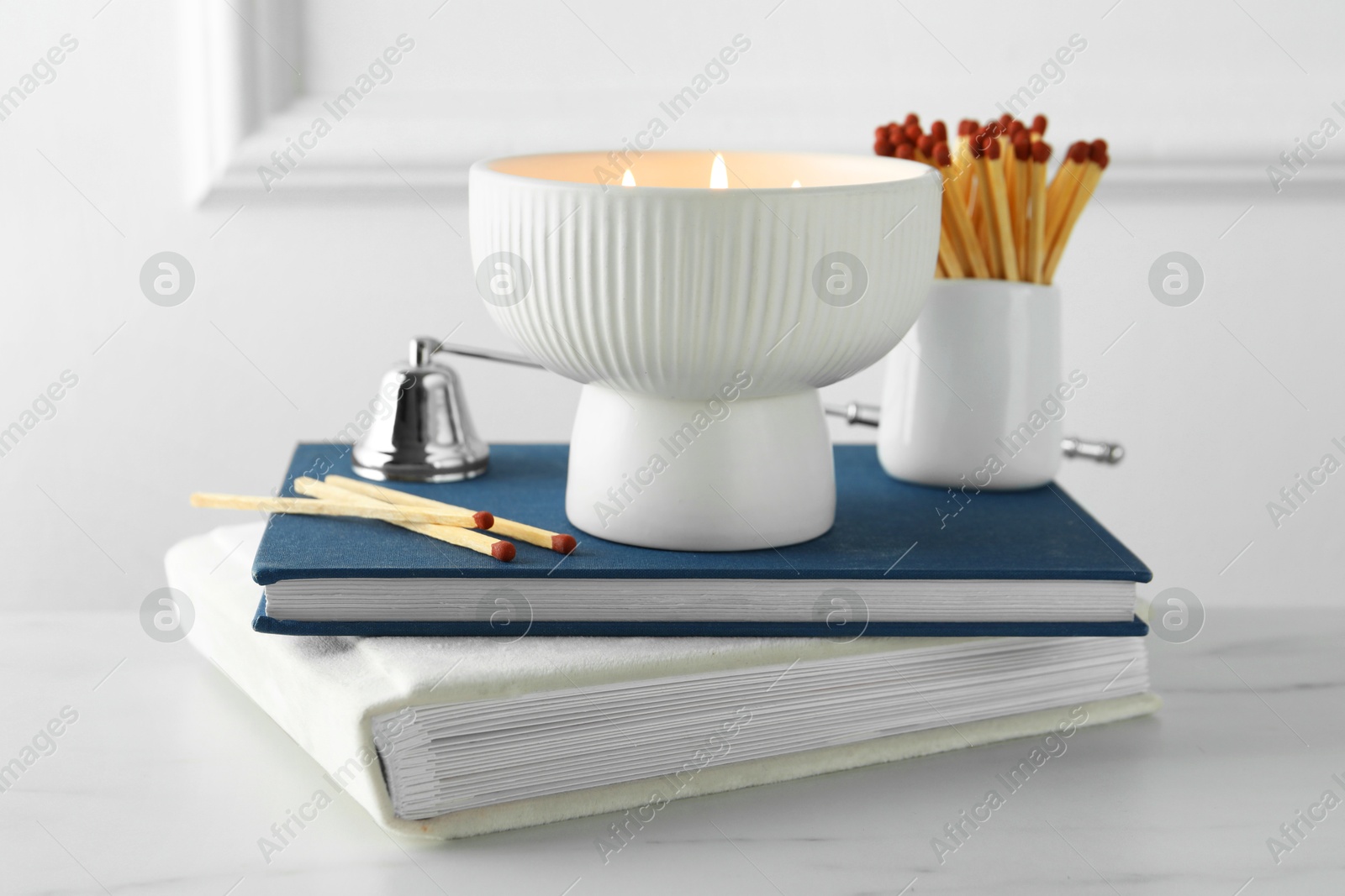 Photo of Burning candle, matches, books and bell on white marble table, closeup