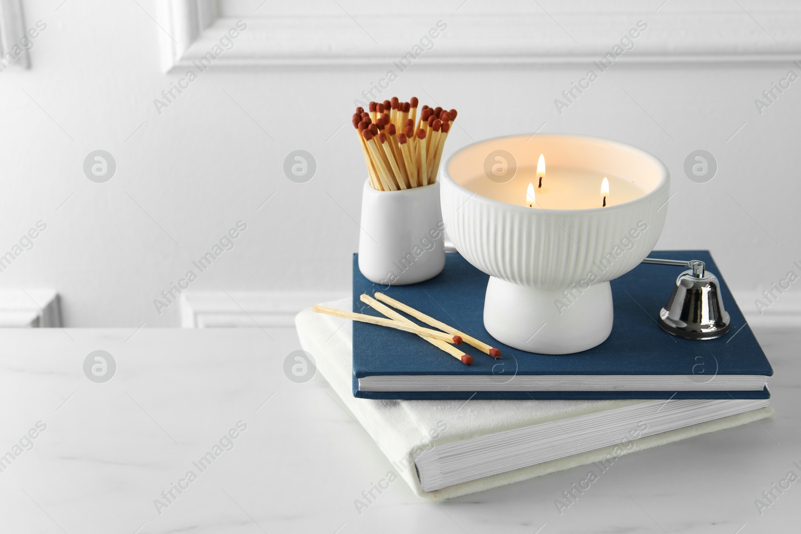 Photo of Burning candle, matches, books and bell on white marble table, space for text