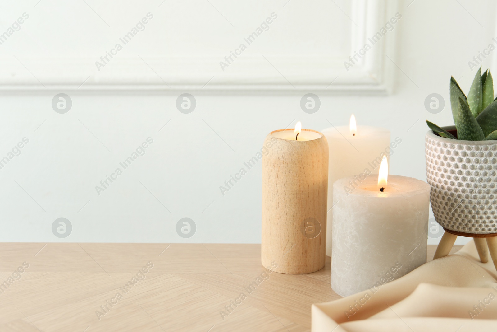 Photo of Beautiful burning candles, houseplant and cloth on wooden table, closeup. Space for text