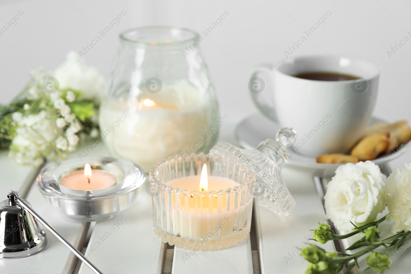 Photo of Beautiful burning candle, tea and flowers on white wooden table, closeup