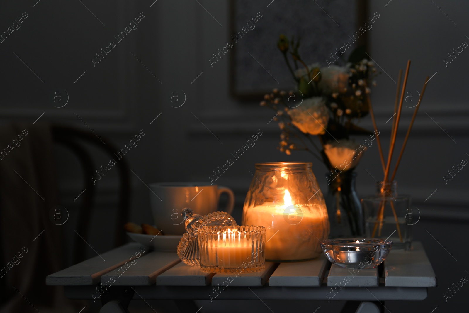 Photo of Beautiful burning candle and flowers on white wooden table