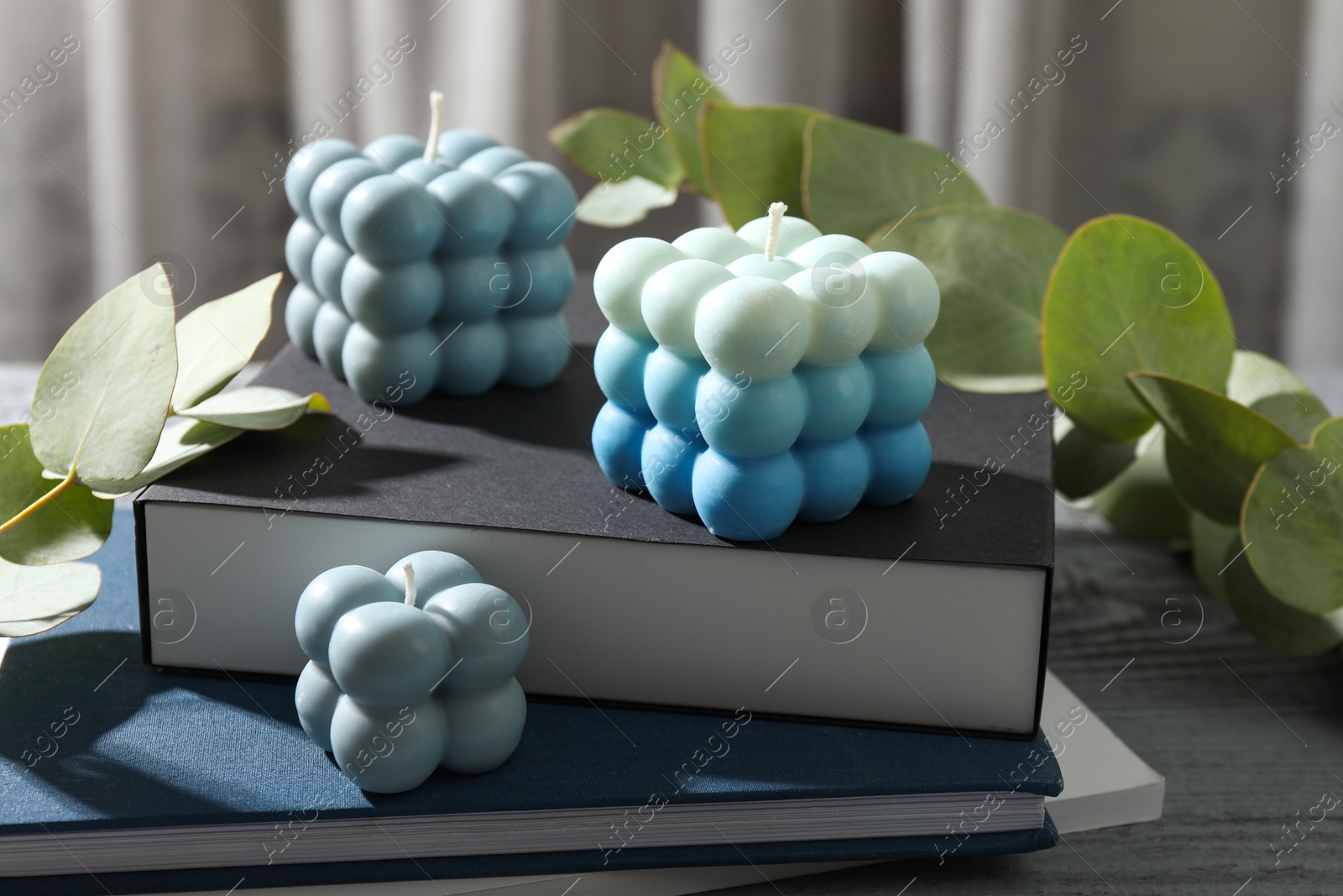 Photo of Stylish bubble candles and stack of books on grey wooden table, closeup