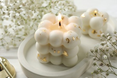 Photo of Stylish bubble candles and gypsophila flowers on white wooden table, closeup