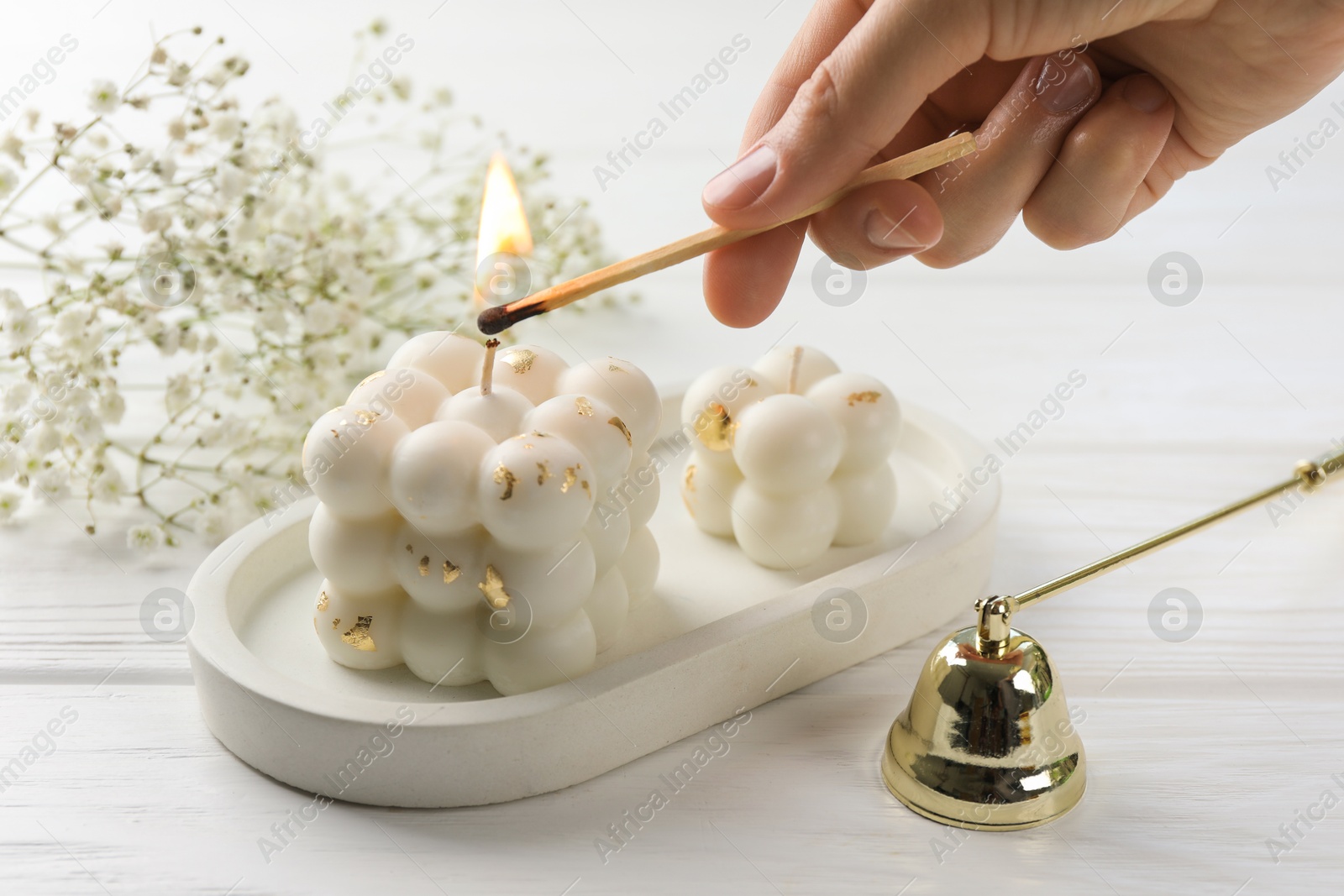 Photo of Woman lighting bubble candle with match at white wooden table, closeup