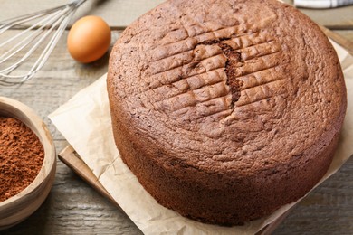 Photo of Tasty chocolate sponge cake, whisk, egg and cocoa powder on wooden table, closeup