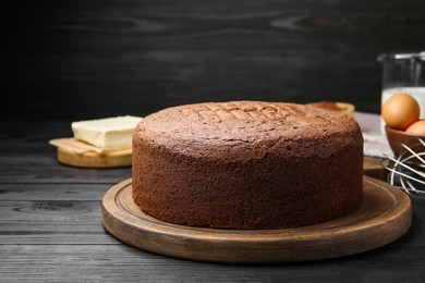 Photo of Tasty chocolate sponge cake and ingredients on black wooden table