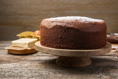 Photo of Tasty chocolate sponge cake with powdered sugar and ingredients on wooden table, closeup